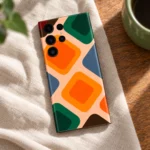 Abstract mobile skin with orange and green rounded diamonds on peach, linen flat lay