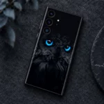 Black owl mobile skin with vivid cyan-blue eyes and charcoal feather artwork, graphite flat lay view