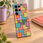 Colourful patchwork mobile skin with floral panels, polka dots, stripes and printed stitch borders, creative desk lifestyle view