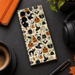 Halloween pattern mobile skin with pumpkins, witch hats and black cats on cream, charcoal desk flat lay view
