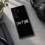 Black I'm Fine mobile skin with white distressed lettering, headphones desk view