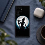 Black Krishna full moon mobile skin on blue linen beside notebook and earbuds case