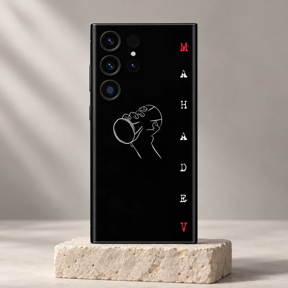 Black Mahadev Damru mobile skin with white line art and red letters on a pale stone pedestal