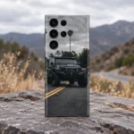 Black off-road SUV mobile skin with palm trees, a cloudy sky and yellow road lines, outdoor slate setting