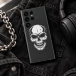Minimal White Skull Mobile Skin with white skull artwork on charcoal grey, black denim flat lay