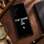 Black The Game Is On mobile skin with white quote and detective silhouette, walnut chess flatlay