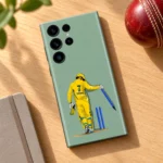 Dhoni vector phone skin displayed diagonally on an oak desk beside a cricket ball