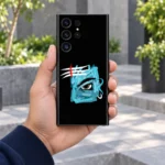Handheld black Mahadev phone skin with blue eye brushstroke artwork in a grey courtyard