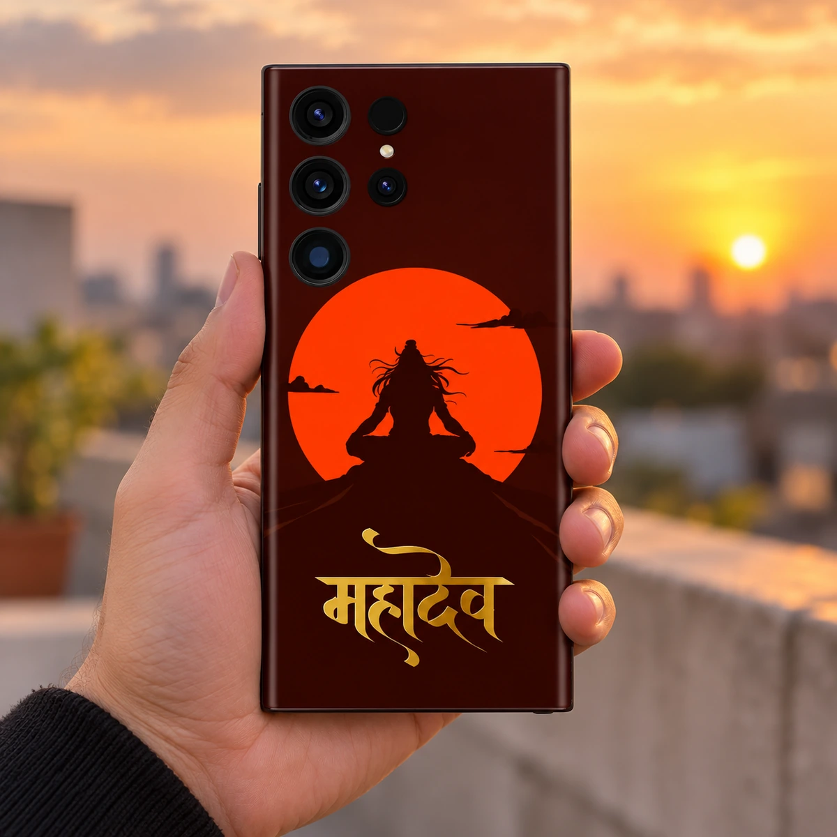 Mahadev Orange Sun Gold Script Mobile Skin - In Hand Mahadev orange sun mobile skin held in hand on a rooftop at sunset