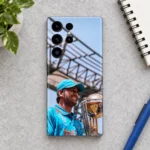 MS Dhoni trophy photo mobile skin with blue jersey and cap, daylight desk flat lay