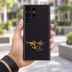 Radhe Radhe mobile skin with gradient Hindi calligraphy on charcoal black, in-hand lifestyle