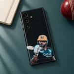 Virat Kohli mobile skin with gold helmet and bat portrait on black, teal desk flat lay
