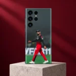 Virat Kohli walking in red and black cricket kit on a phone skin, burgundy studio portrait