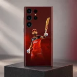 Virat Kohli mobile skin with raised bat and red cricket kit against burgundy, charcoal plinth hero