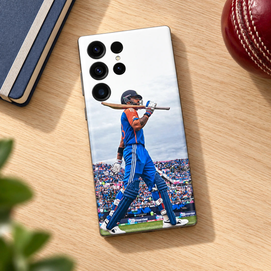 Virat Kohli Bat-on-Shoulder Mobile Skin – Oak desk flat lay Virat Kohli mobile skin with blue kit and bat across shoulders, oak desk flat lay