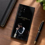 Black Virat Kohli mobile skin with gold 1% chance quote and seated portrait, walnut desk flat lay