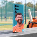 Virat Kohli smiling in an orange training shirt on a teal mobile skin, practice pavilion