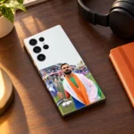 Virat Kohli trophy mobile skin lying on a walnut desk beside headphones and an orange notebook