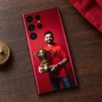 Virat Kohli smiling with a gold trophy against red on a mobile skin, walnut flat lay
