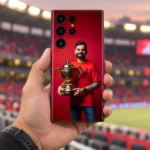 Virat Kohli smiling with a gold trophy against red on a mobile skin, stadium hand-held view