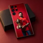 Virat Kohli smiling with a gold trophy against red on a mobile skin, burgundy studio detail