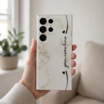 Elegant Marble Customized Name Mobile Skin — in hand showing cream marble with black hearts and custom cursive name