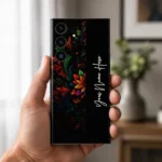 Royal Floral Glow Customized Name Mobile Skin — in hand showing colourful floral scrollwork on black with vertical white cursive sample name