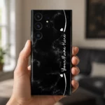 Black Marble Custom Name Mobile Skin — in hand showing black marble with subtle grey veins, white hearts and cursive sample name