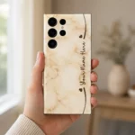 Cream Marble Custom Name Mobile Skin — in hand showing warm cream marble with brown hearts and cursive sample name