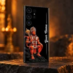 Black custom name mobile skin with seated orange Hanuman and golden gada in warm saffron studio light