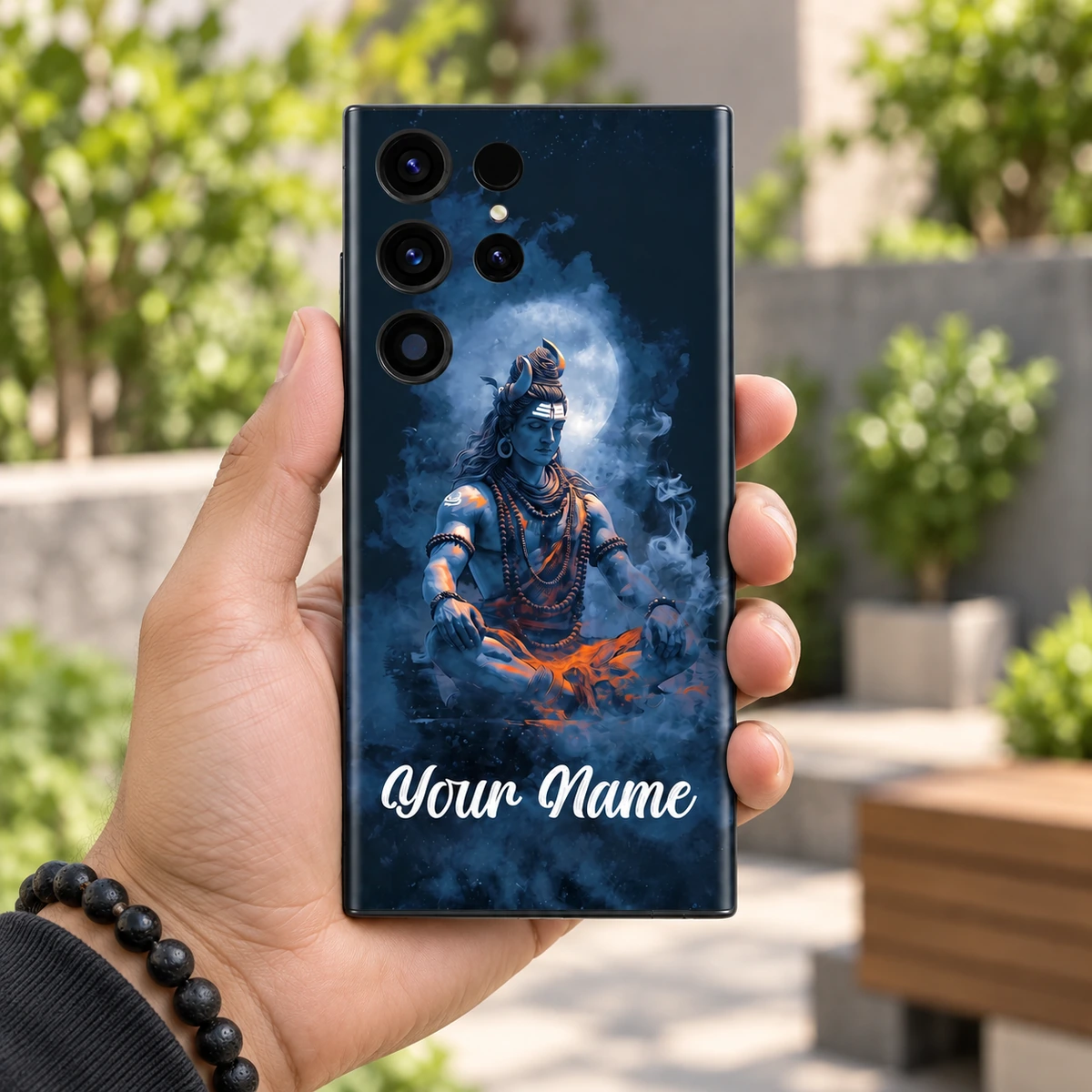 Lord Shiva Moonlight Custom Name Mobile Skin - Daylight handheld Lord Shiva blue meditation custom name skin held in hand in a garden courtyard